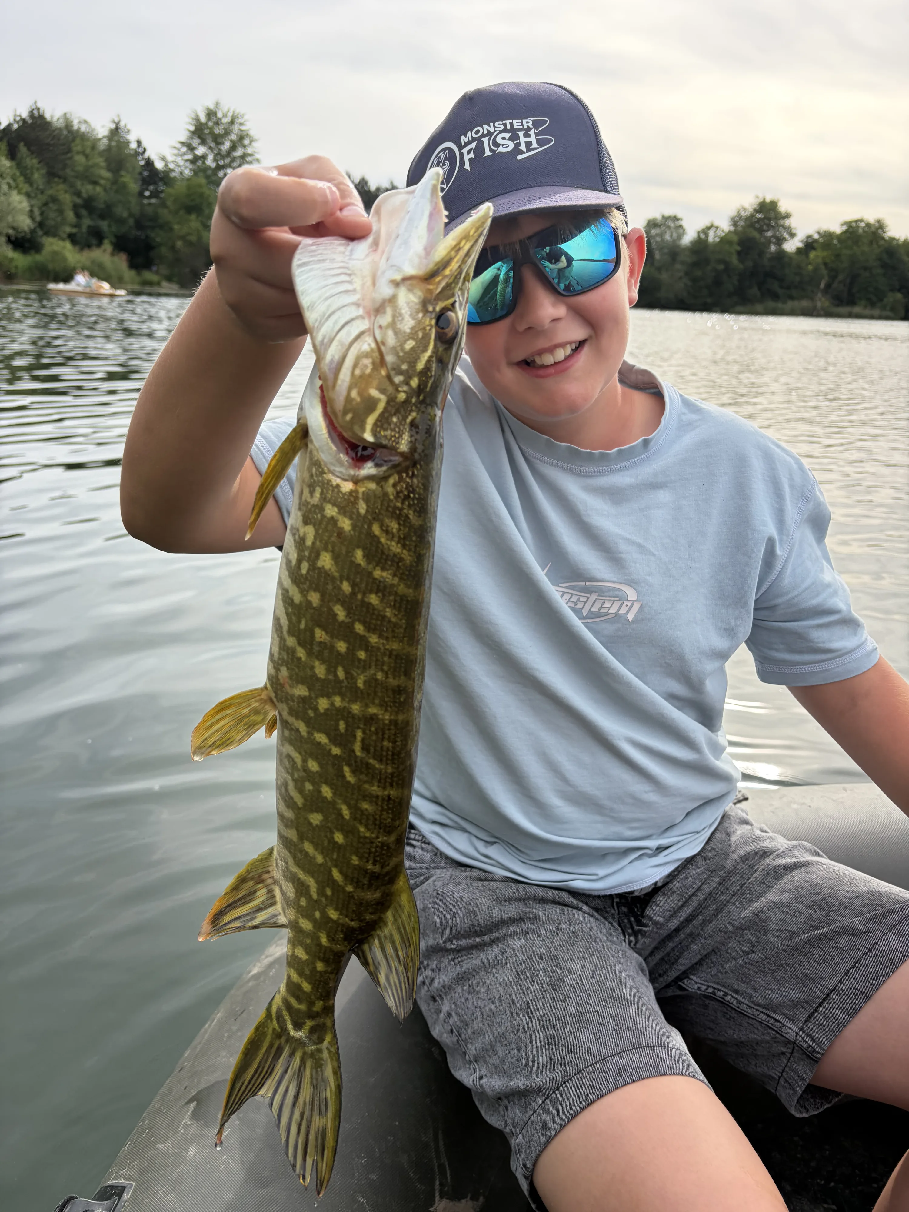 Junger Angler mit seinem Hecht im Boot