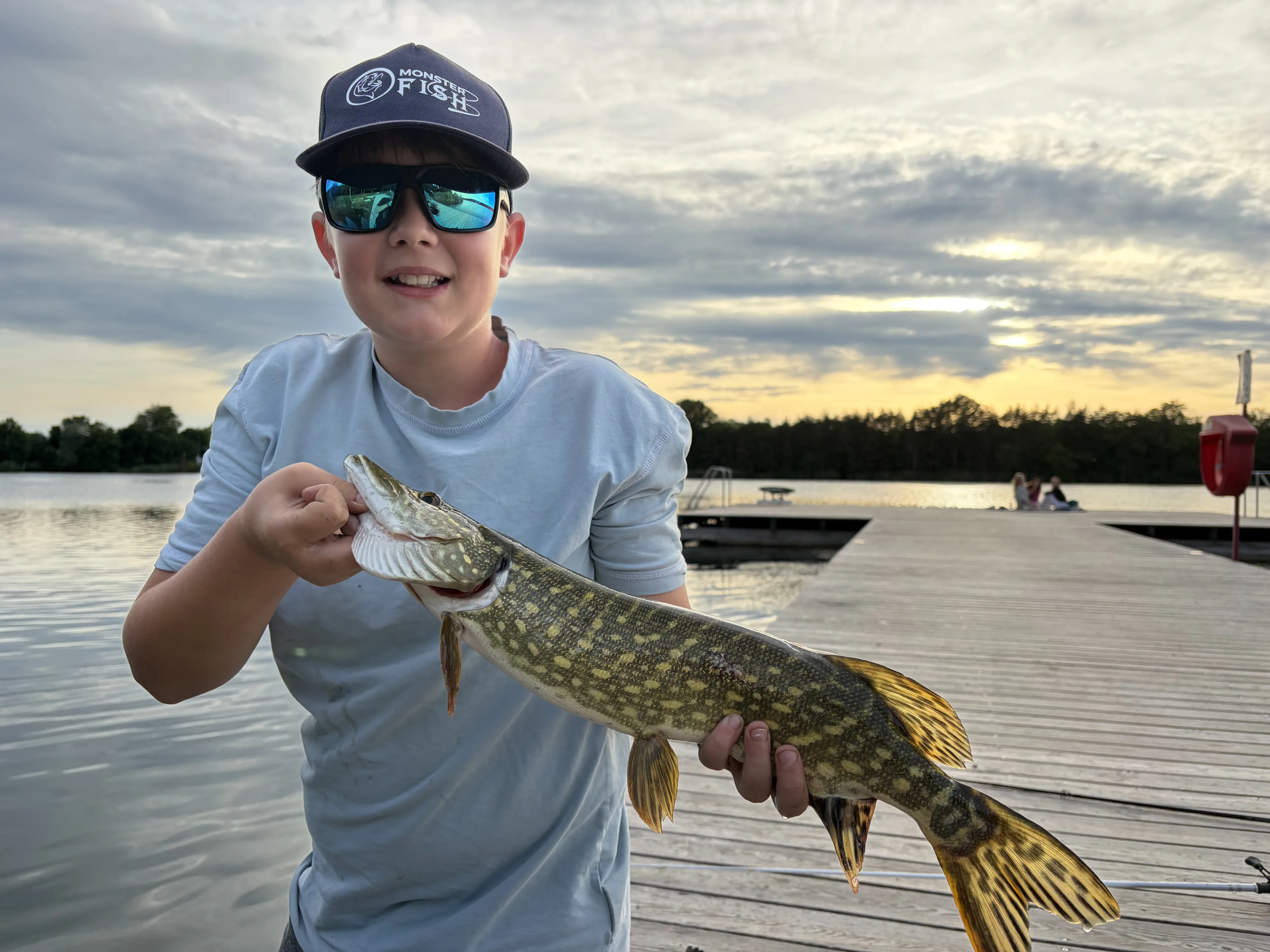 Junger Angler mit Hecht am Steg im Abendlicht