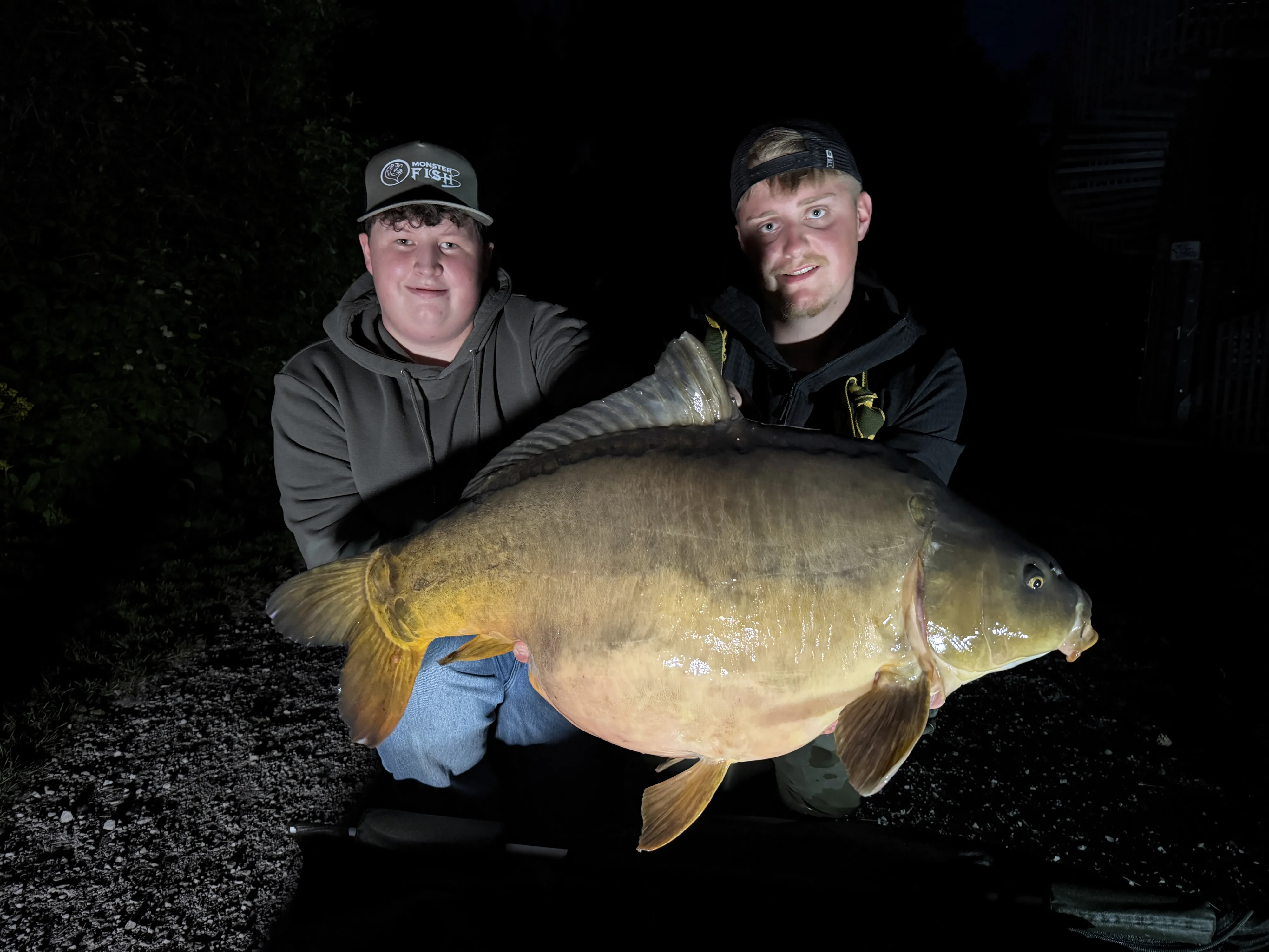 Zwei Angler mit einem großen Spiegelkarpfen beim Nachtangeln